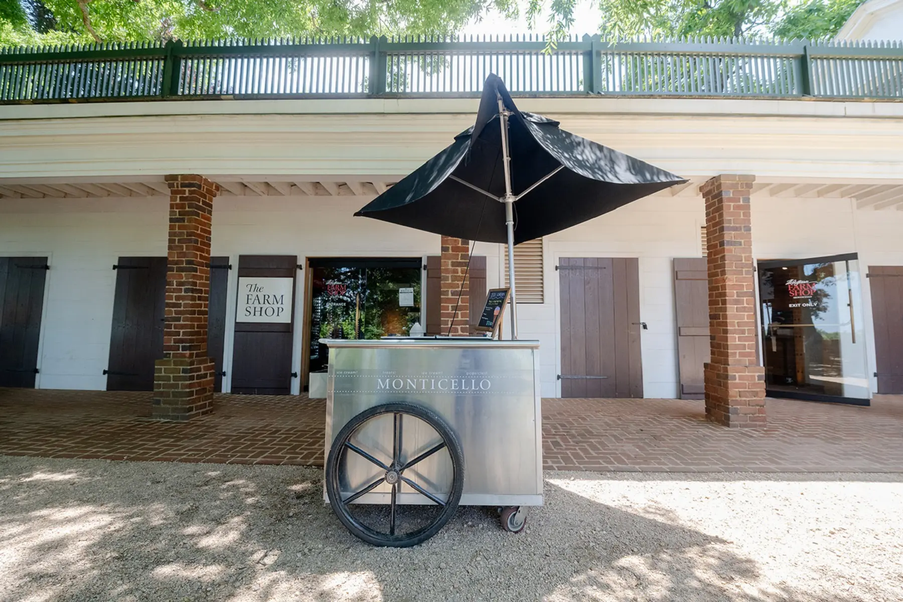The exterior of the Monticello Farm Shop in the North Wing of the main house with an ice-cream cart adorned with an umbrella out front.