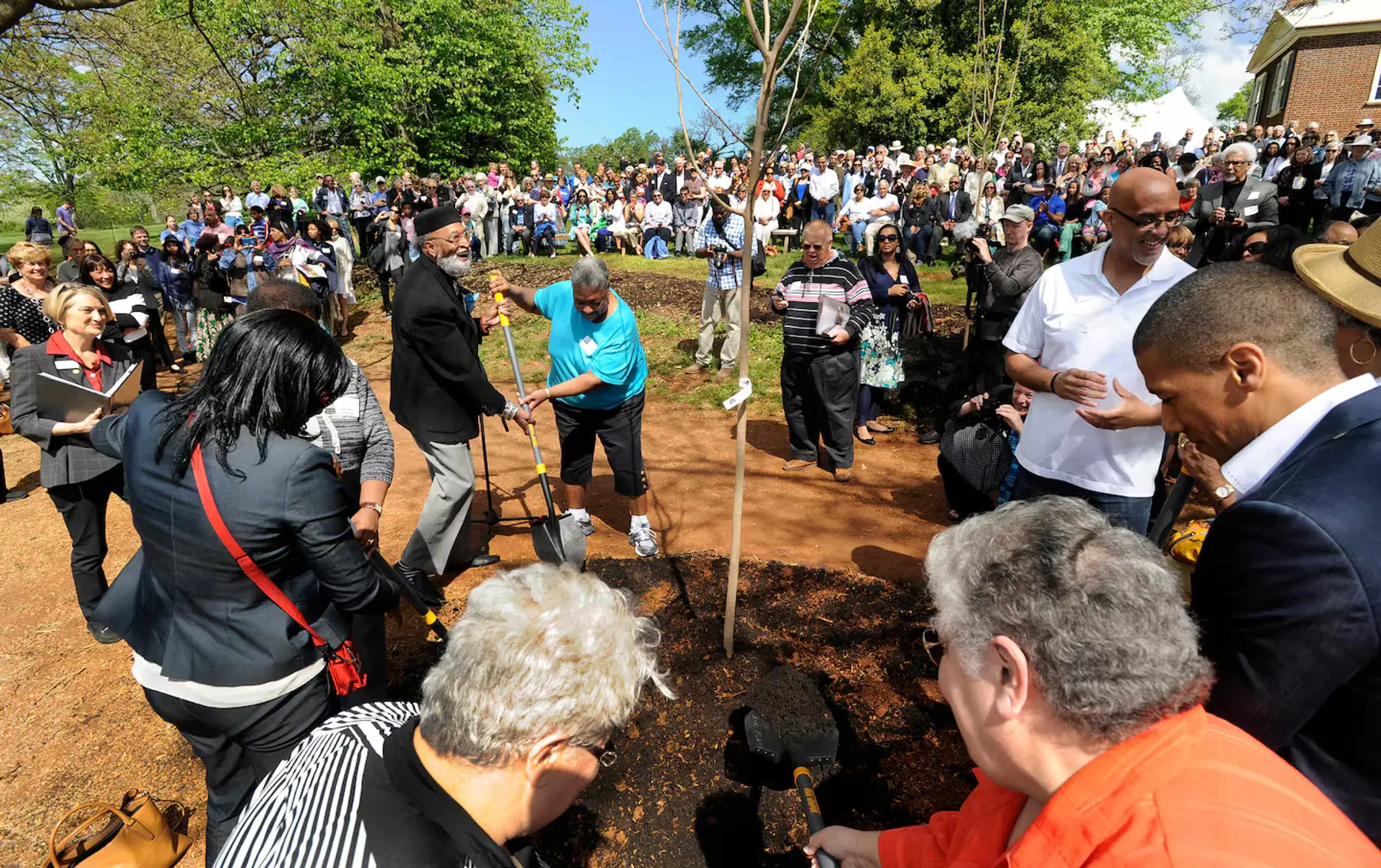 Men and women from Monticello's descendant community shovel dirt around a tree planting while over a hundred people look on.