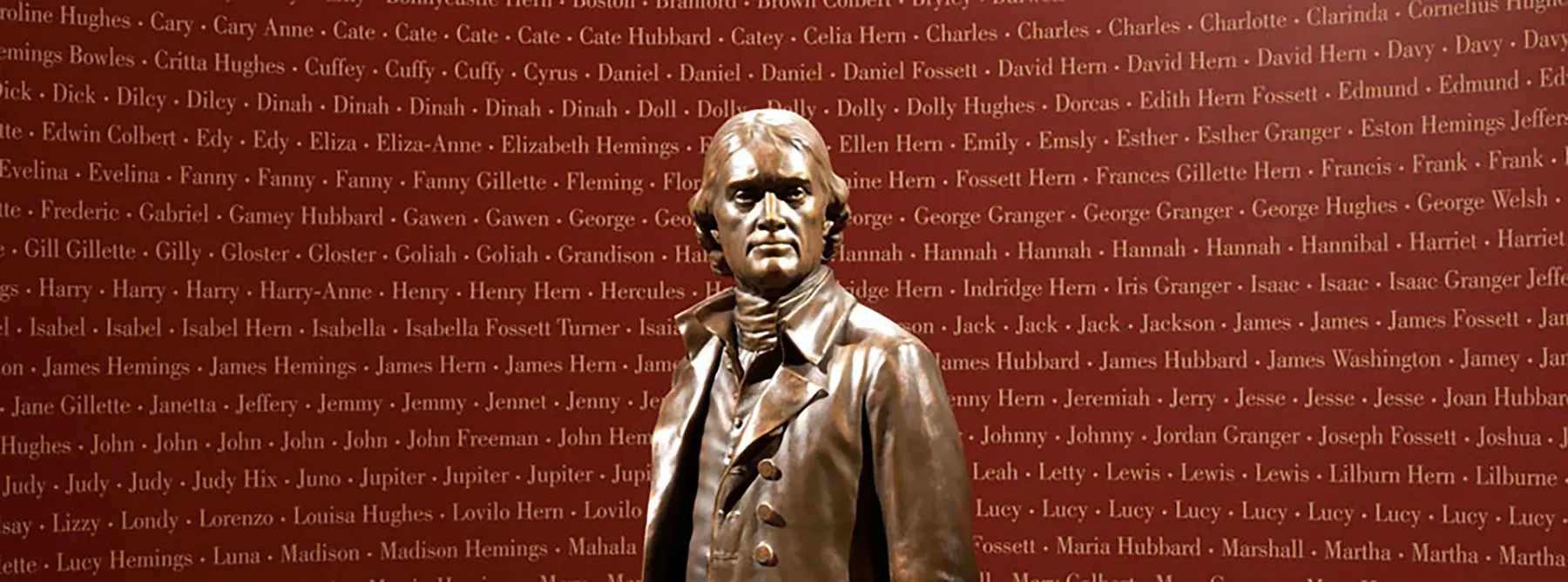Bronze statue of Thomas Jefferson in front of a red wall covered in the names people enslaved at Monticello and other Jefferson plantations.